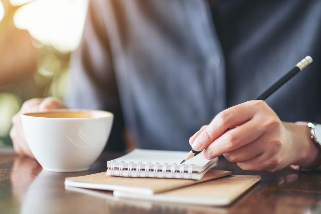 Closeup image of a woman holding a notebook and coffee cup